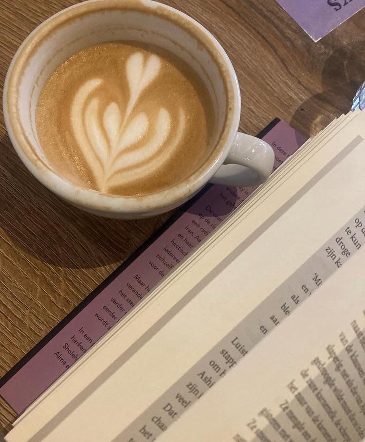 Een kop koffie naast een opengeslagen boek op een houten tafel